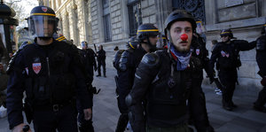 Links ein Polizist mit Schutzhelm, rechts ein Demonstrant mit roter Nase