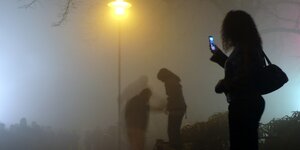 Die Silhouette einer Frau mit Mobiltelefon im Nebel