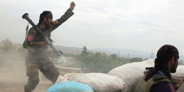 Ein Soldat mit einem Raketenwerfer auf der Schulter hebt den linken Arm in Jubel, rechts im Bild der Hinterkopf eines weiteren Menschen