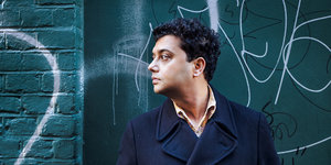 Der Autor Neel Mukherjee seitlich im Profil vor einer Wand mit Graffitti