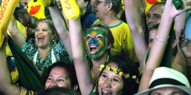 Menschen sind in den Farben der brasilianischen Flagge gekleidet und feiern, eine Frau ist in grün-gelb geschminkt