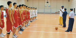 Zwei Basketballmannschaften stehen in einer Halle vor drei Männern