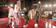 Eine Frau im Minirock steht mit einem Mann auf der Theaterbühne, neben ihr eine überlebensgroße Katze mit Sprengstoffgürtel