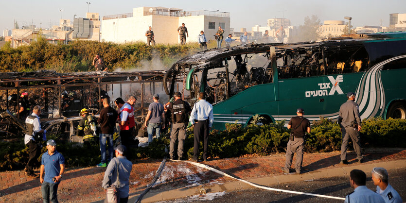 Ein ausgebrannter Bus ist von Menschen umringt