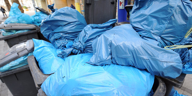 Blaue Müllsäcke quellen aus übervollen Tonnen.