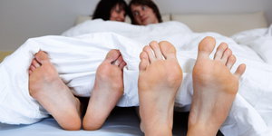 Ein junges Paar schmust zusammen verliebt im Bett, dabei schauen die Füße raus