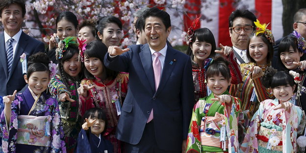 Japans Premier Shinzo Abe und als Geishas verkleidete Mädchen zeigen beim Kirschblütenfest in die Kamera