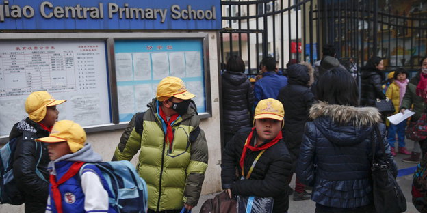 Kinder werden von ihren Eltern vor einer Schule abgeholt, manche tragen Schutzmasken gegen den Smog