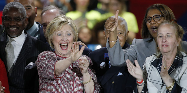 Hillary Clinton winkt und jubelt, umringt von klatschenden UnterstützerInnen