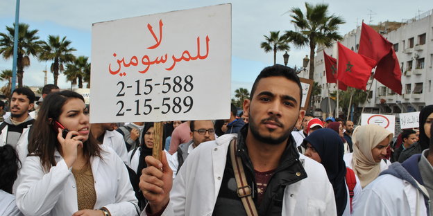 Ein junger Mann hält ein Schild mit dem Schriftzug "Nein zu den beiden Verordnungen", im Hintergrund mehr Protestierende