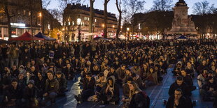 Viele Menschen sitzen und stehen abends auf einem Platz