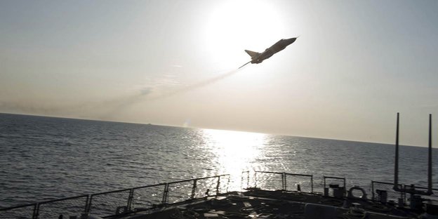 Ein Kampfflugzeug fliegt über einem Schiff vor der Sonne