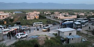 Ein Dorf in der Dämmerung. Fahrzeuge und Menschen sind auf der Straße