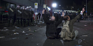 Zwei Männer sitzen am 1. Mai auf der Straße am Kottbusser Tor in Berlin vor einer Gruppe Polizisten und strecken die Hande zum Viktory-Zeichen in die Höhe