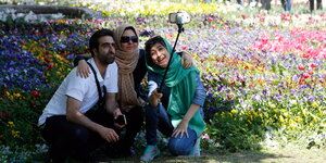 Mann im T-Shirt und zwei Frauen mit Kopftuch machen ein Selfie bei der Blumenausstellung in Karaj, Iran, April 2016