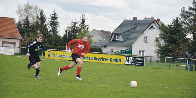 Zwei Fußballer in unterschiedlichen Trikots rennen auf einem gepflegten Rasenplatz hinter einem Ball her