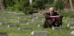 Ein Mann sitzt im Gras zwischen Grabsteinen