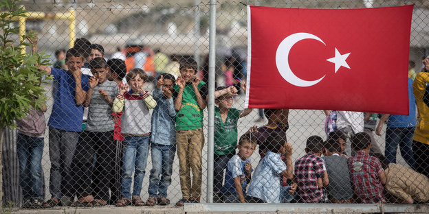 Kinder stehen hinter einem Zaun, an dem die türkische Flagge hängt