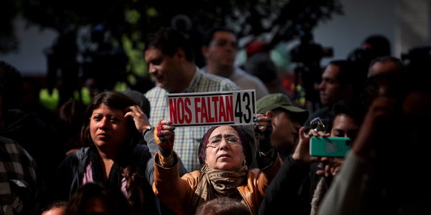 Eine Frau hält ein Schild hoch auf dem auf Mexikanisch steht „Wir vermissen die 43“