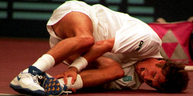 Michael Stich liegt im weißen Tennisdress am Boden und hält sich schreiend den Knöchel