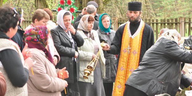 Ein orthodoxer Priester und andere Menschen auf einem Friedhof