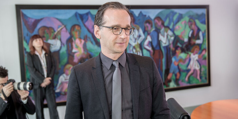 Heiko Maas vor einem bunten Bild, schräg hinter ihm ein Fotograf