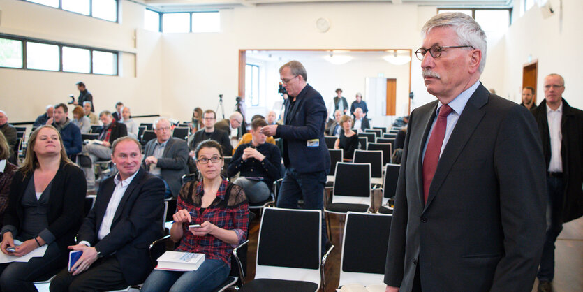 Thilo Sarrazin steht im Anzug vor halb besetzten Stuhlreihen