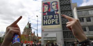 Ausgestreckte Mittelfinger vor einem Obama-Merkel-Plakat