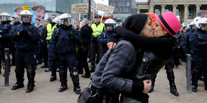 Zwei Frauen küssen sich, dahinter steht eine Reihe Polizisten