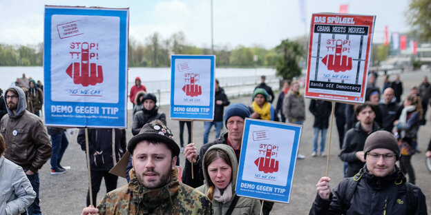 Protest gegen TTIP: Junge Menschen halten Plakate hoch, auf denen eine rote Hand zu sehen ist, die den Stinkefinger zeigt