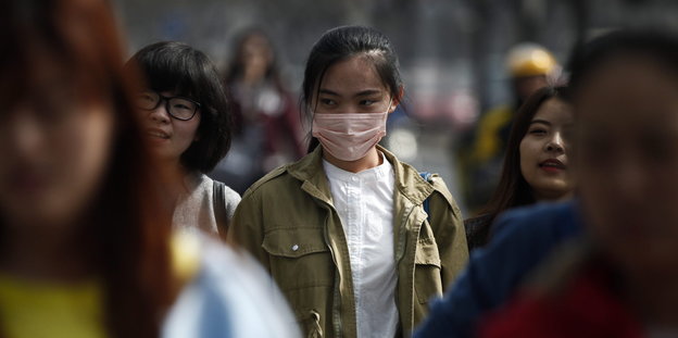Eine Frau mit Atemschutzmaske zwischen Passanten in Peking