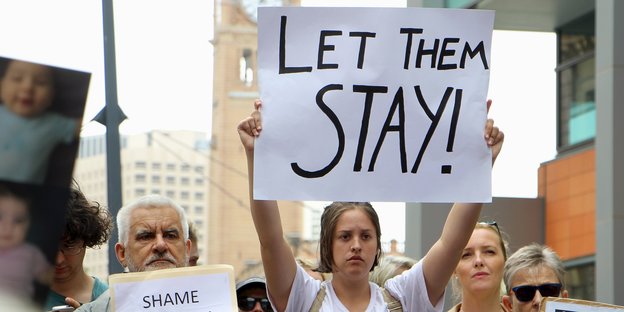 Eine Demonstrantin hält ein Schild hoch, auf dem steht "Let them stay"