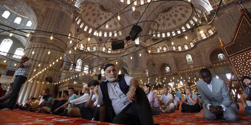 Männer sitzen auf Teppichen in einer Moschee