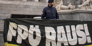 Ein Polizist steht hinter einem Banner mit der Aufschrift "FPÖ RAUS!"