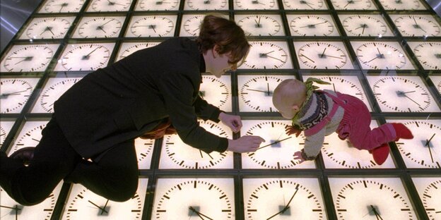 Eine Frau und ein Baby sitzen auf einem Boden, der aus von unten beleuchteten Uhren besteht