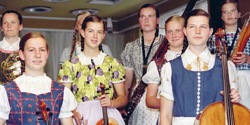 Mädchen in Trachten, alle haben geflochtene Zöpfe und ein Musikinstrument in der Hand