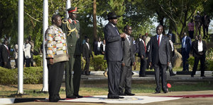 Riek Machar und Salva Kiir und weitere Männer in Anzügen und Uniformen stehen still und hören der Nationalhmyne zu