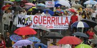 Menschen tragen bunte Regenschirme und ein Transparent gegen die Farc