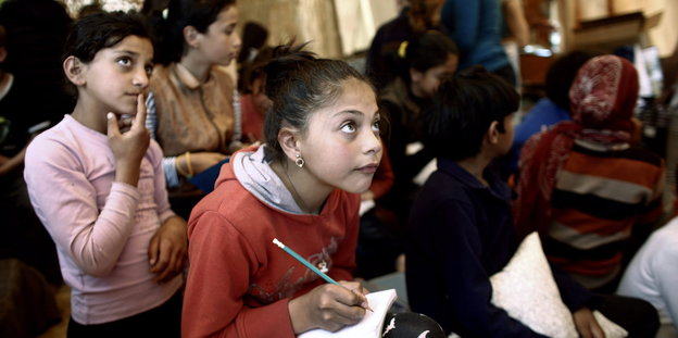 Flüchtlingskinder sitzen dicht gedrängt in dem provisorischen Klassenraum, Stift und Papier in der Hand, den Blick konzentriert nach vorne gerichtet