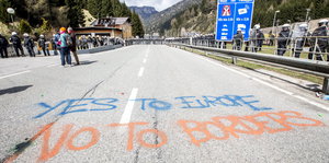 Straße mit dem Graffito „Yes to Europe – no to borders“, daneben Polizisten in riot gear, im Hintergrund Berge