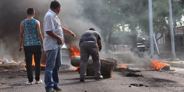 Drei Menschen stehen vor einer brennenden Barrikade