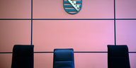 Drei Stühle vor einer Wand, an ihr hängt ein Wappen