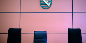 Drei Stühle vor einer Wand, an ihr hängt ein Wappen
