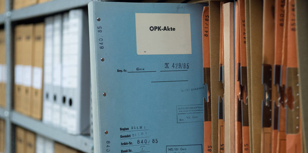 Eine hellblaue Stasi-Akte mit der Aufschrift "OPK" steckt in einem Regal