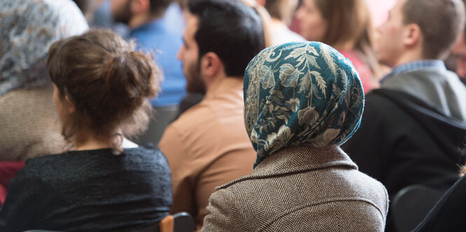 Menschen mit und ohne Kopftücher sitzen zusammen im Publikum