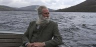 Ein Mann mit Bart sitzt mit gefalteten Händen in einem Boot auf Loch Ness