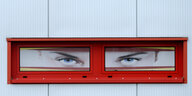Eine mit Augenplakaten dekorierte Fensterfront an einem Gebäude