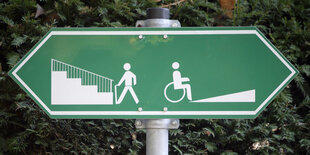 Schild, das in zwei Richtungen weist. Auf der linken Seite ist eine Treppe, auf der rechten eine Rampe.