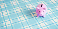 Ein rosafarbenes Sparschwein steht auf einer blau karierten Tischdecke