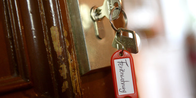 Ein Schlüssel mit Schlüsselanhänger, auf dem “Ferienwohnung“ steht, steckt in einer Tür